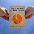 Two hands holding 'The London Coffee Guide' against a blue sky