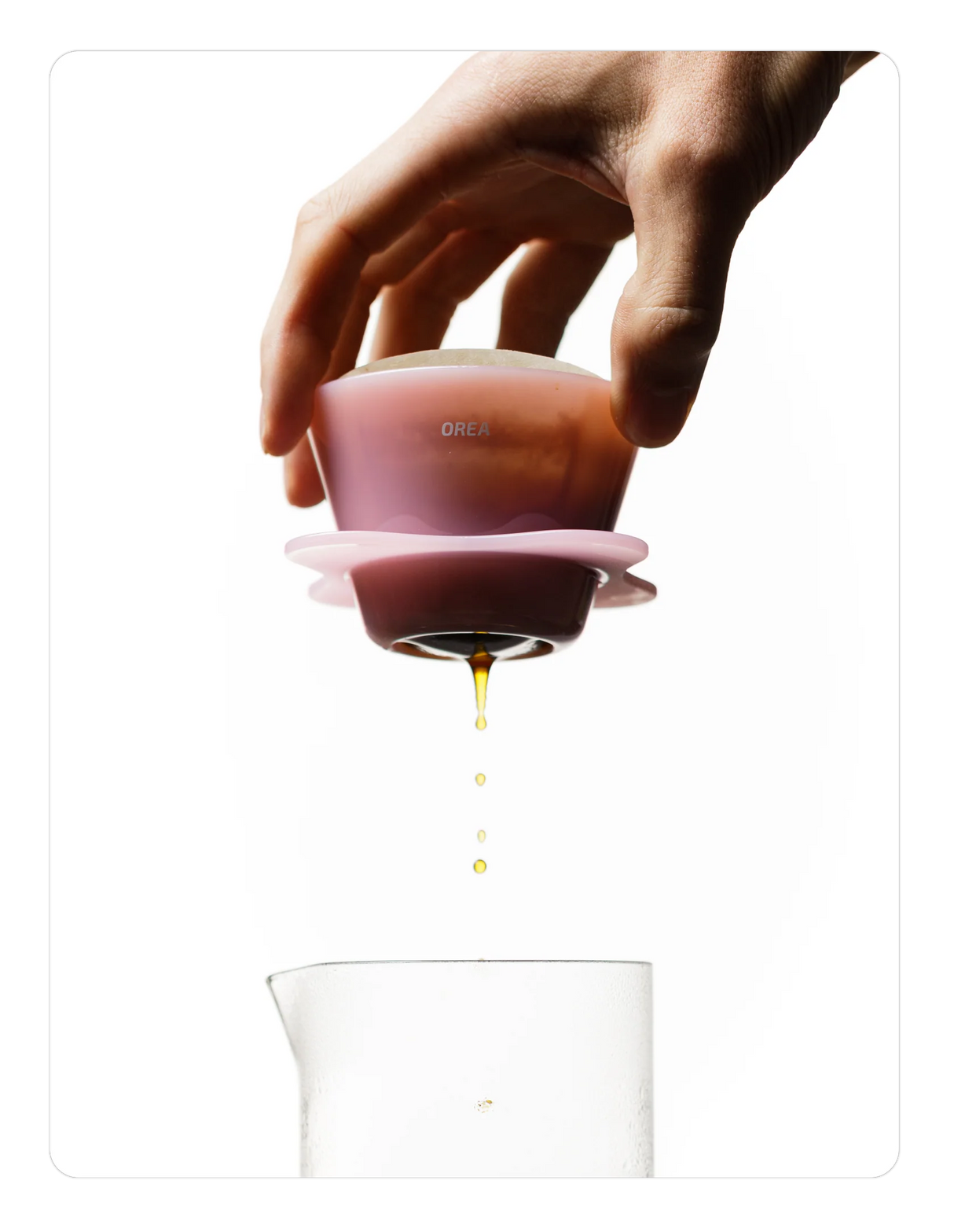 Hand holding a Creamy pink OREA 01 brewer with a clear container below on a white background