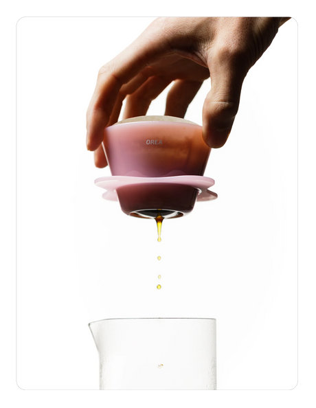 Hand holding a Creamy pink OREA 01 brewer with a clear container below on a white background